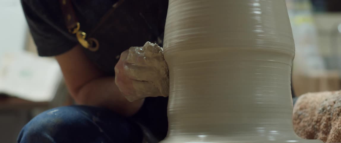 Large piece of wet clay spins as it is being sculpted by a clay covered hand