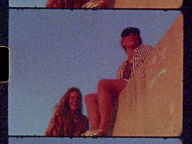 Friends sit on paint smeared wall under a clear sky as they laugh and talk