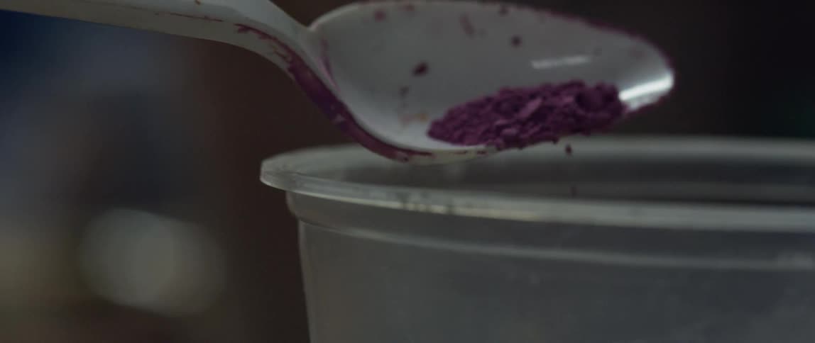 A person is pouring purple powder into a cup