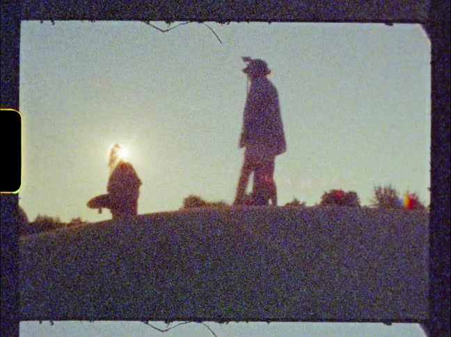 Silhouette of two girls with skateboards standing on a hill in front of the sun