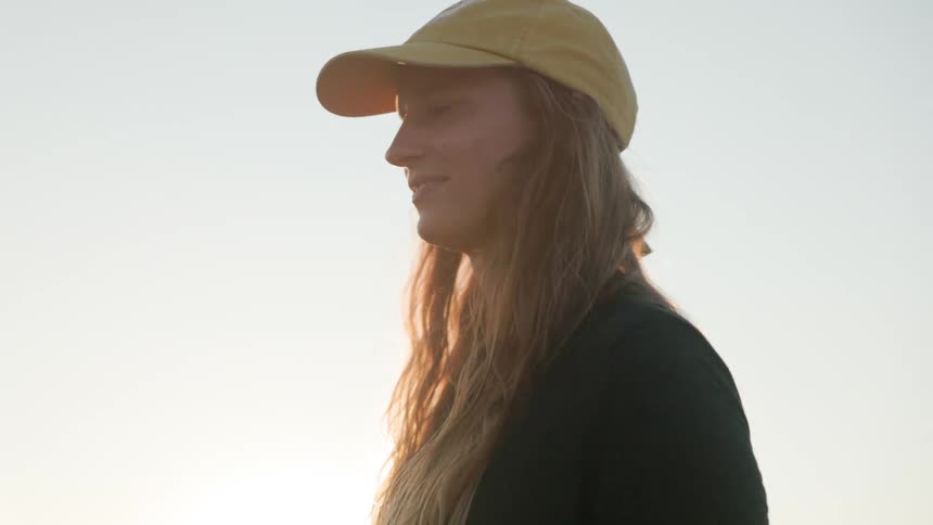 A woman with long hair wearing a baseball cap smiles in the sunshine