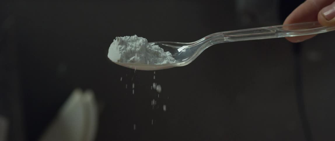 A woman shakes flour off of a plastic spoon