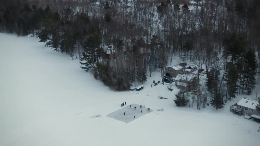 A group of people are outside playing hockey on a winter day and others are watching