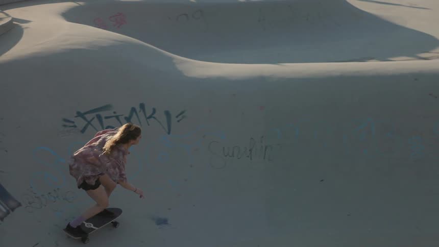 A teenage girl skateboards up and down slopes at a skateboard park