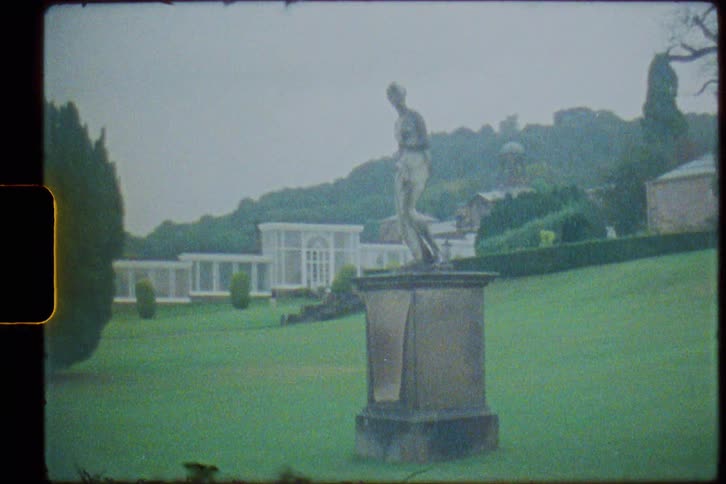 Statue of woman stands on pedestal on lawn of estate on misty day