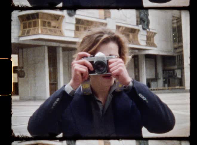 A man standing in a plaza taking a photograph with a landmark building behind him