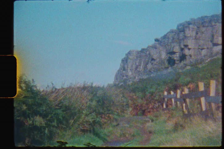 A cliff looming over a hilly grassland on a sunny day