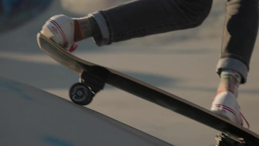 Skateboarder wearing white shoes with red trim rides a skateboard down a skateboard ramp on a sunny day