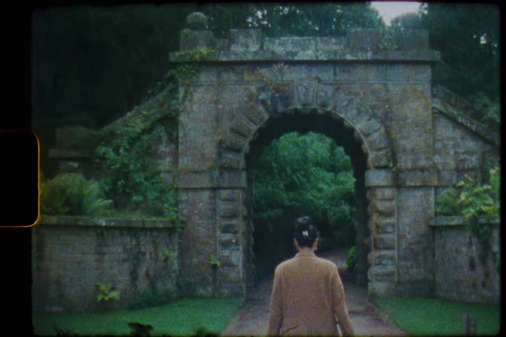 A woman walks toward the archway at the great conservatory in the gardens at chatsworth derbyshire