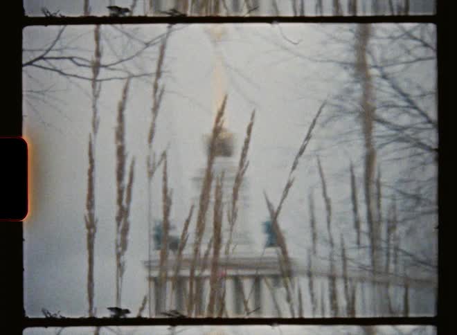 Zoom in the top of a monument behind tall grass caught on vintage film