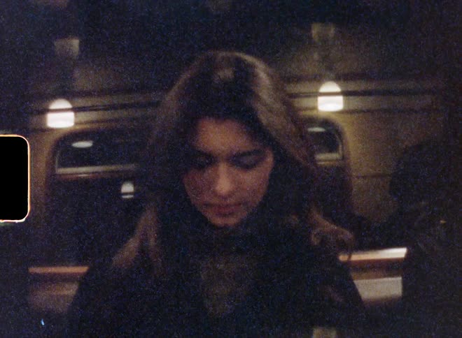 Woman with wavy hair gray sweater and black overcoat uses smartphone in subway station