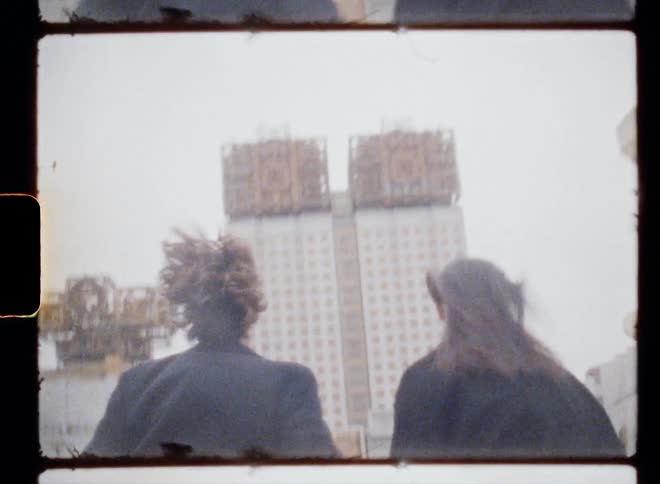 Couple runs hand in hand toward building topped with abstract metal sculpture