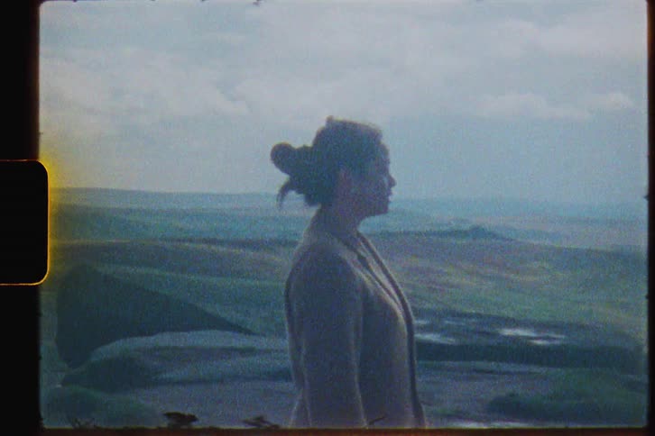 Woman stands near large flat rocks and looks out at the mountains on a breezy day