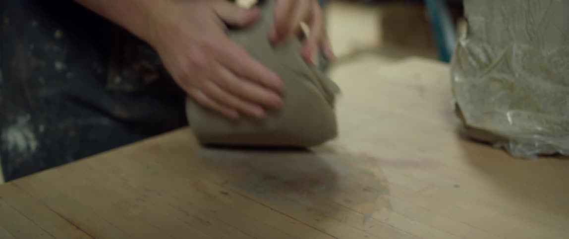Sculptor uses string to slice a piece of clay from a larger piece then rolls it on a wooden table