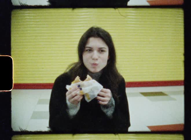 Woman with wavy hair gray sweater and black overcoat eats sandwhich in subway station