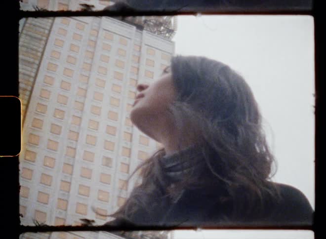 Woman with wavy hair and black overcoat looks up at high rise building in the city