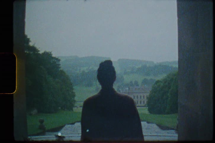 Silhouette of a young woman walking out of a mansion caught on vintage film