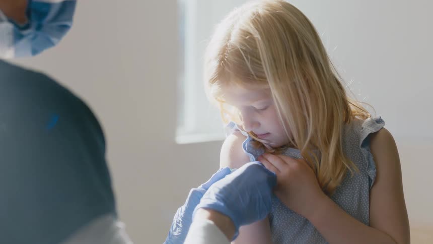 Young girl watches as a nurse puts a band-aid on her arm