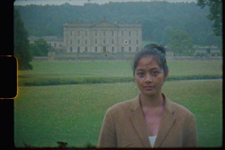Woman stands with river and manor in the background on a misty day