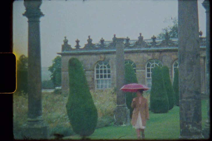 A woman is walking in a garden while holding an umbrella