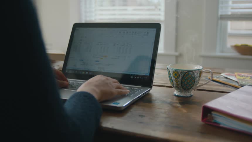 A woman typing on a laptop with a steaming cup of coffee beside her
