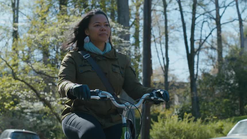 Female bicyclist rides past flowering trees in neighborhood