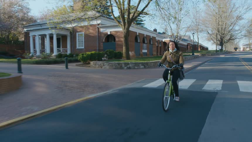 A woman riding a bicycle on campus passing buses