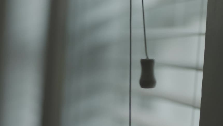 Close up of a hand pulling the control cord of a window shade