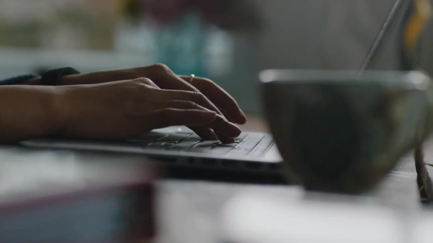 Woman types on laptop with hot cup of coffee