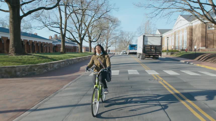 A woman rides a bicycle along college road on a clear day