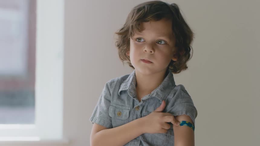 A young boy looks at bandage on his arm after vaccination
