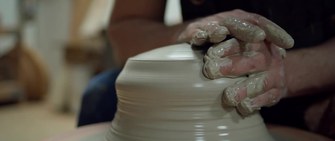 Two hands sculpt the wet clay that is spinning on a pottery wheel