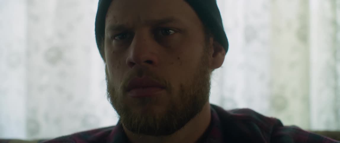 A bearded man looks perplexed before getting up from where he is sitting
