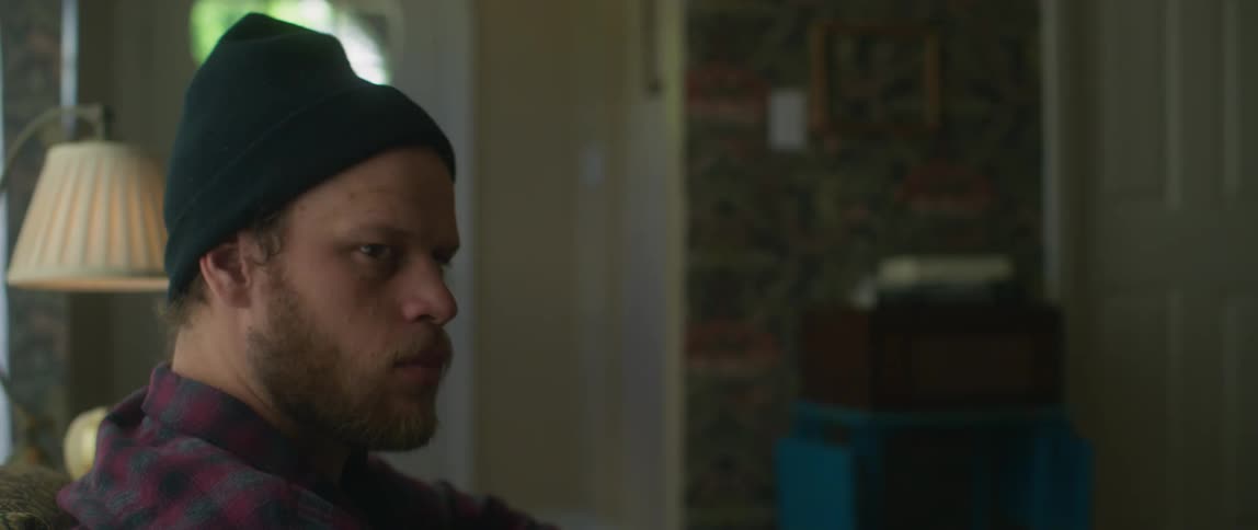 Man wearing a toque turns his head while sitting in a room then rises to a standing position