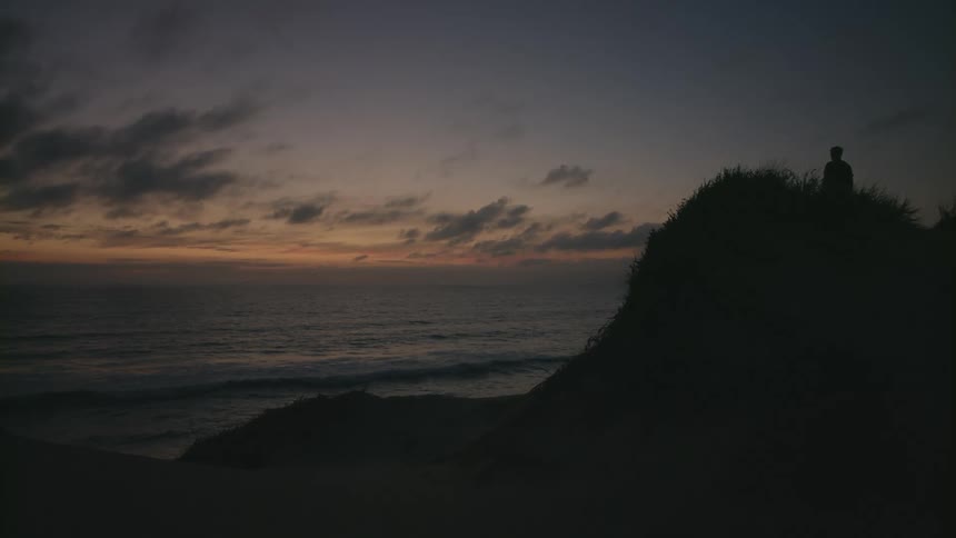 The silhouette of a person standing on a hill overlooking the coast at sunset