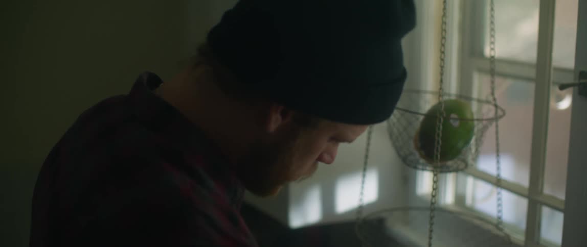 A man standing near the kitchen window looks behind him suddenly then walks away