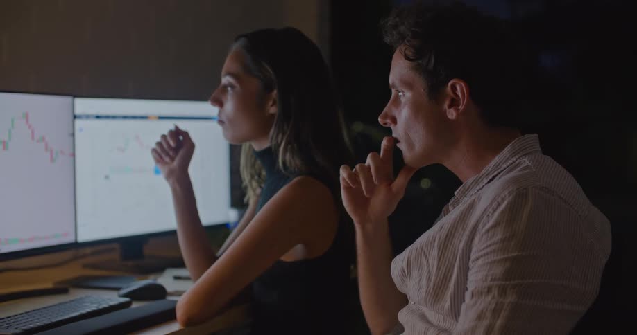 Man and woman sit at a desk and talk as they look at graphics on computer monitors