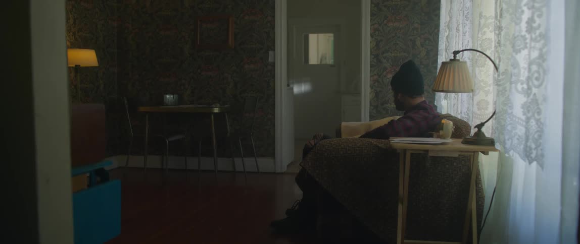 Man wearing a toque uses a remote control to turn off a television while he is sitting on a sofa in a living room