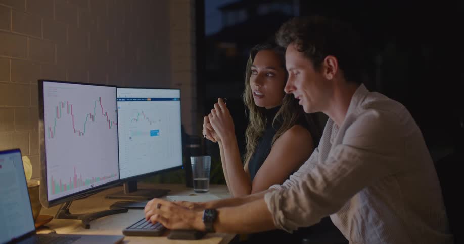Coworkers sit in office discussing graphs on computer screen at night