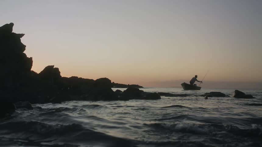 Man stands in a boat in the lake and reaches for a fishing pole
