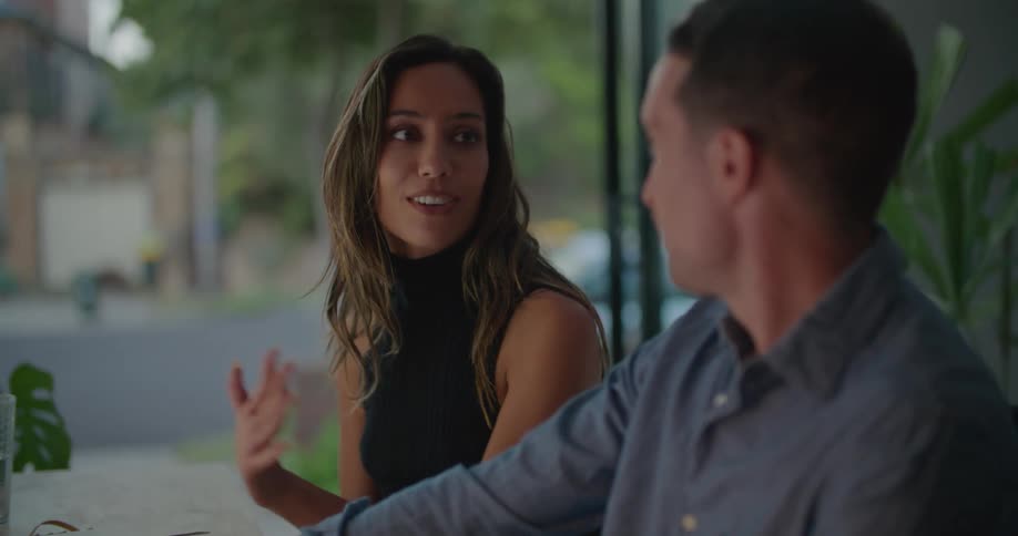 A woman talks with a man as they sit together at a table indoors during the day