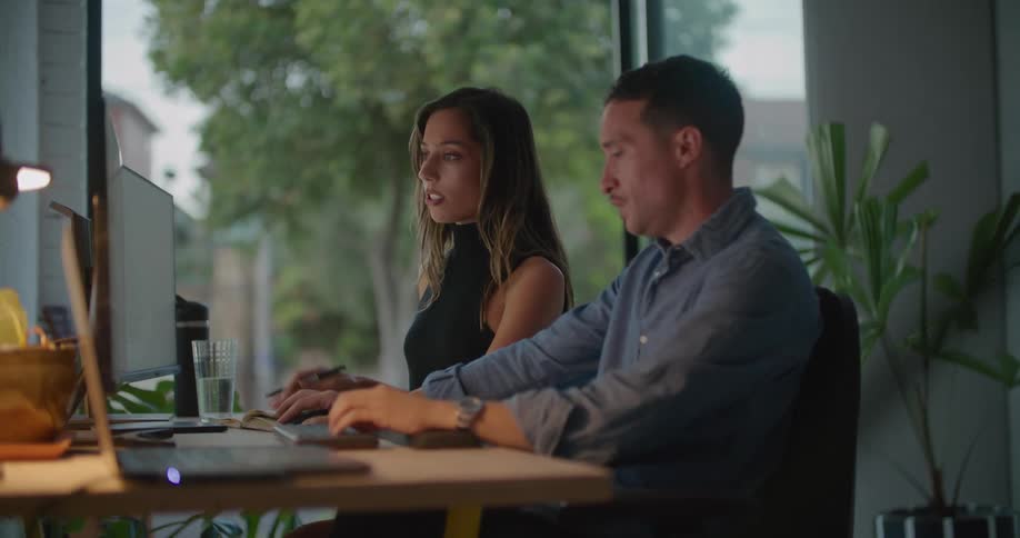 A man and woman sitting at the same desk working and talking together