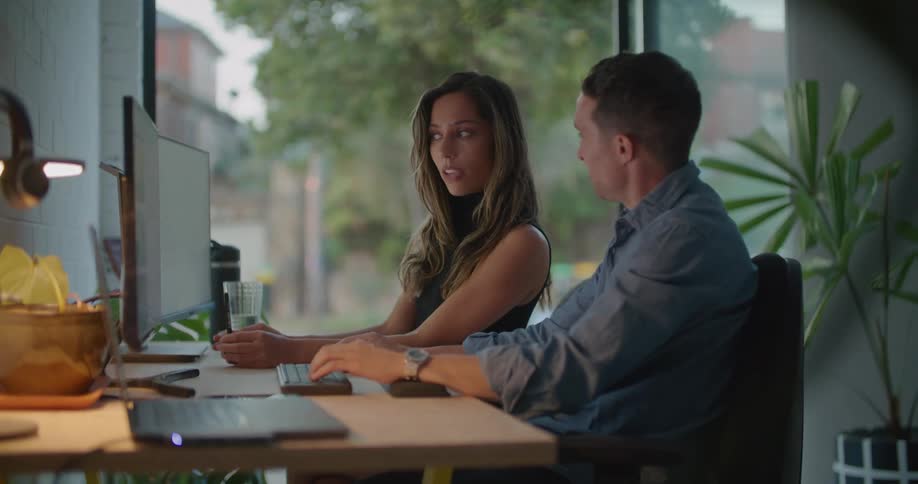 Coworkers discuss data on screen as car pass on road seen through nearby window