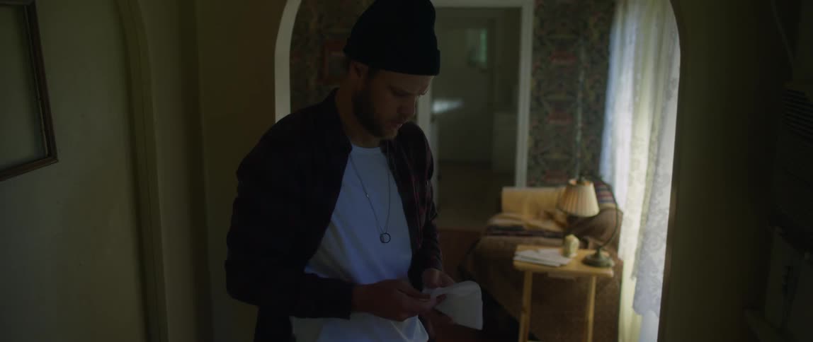 A man is standing indoors and reading a letter