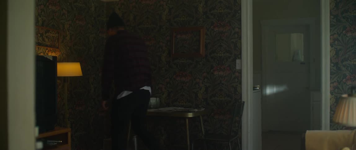 A man walks in to a room in a home and picks up two knocked over chairs as he looks around