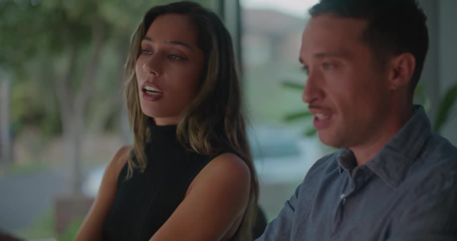 A man and a woman are sitting next to each other and she moves her arms as she talks and they smile and laugh