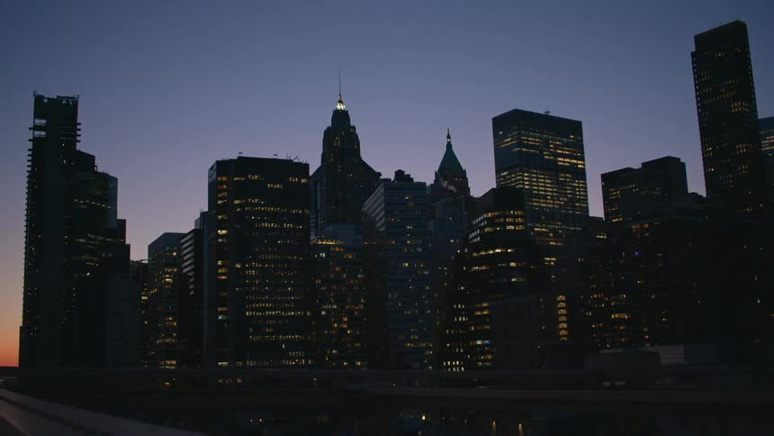 City skyline with tall buildings and towers with spires and lights in the windows as the sky gets darker