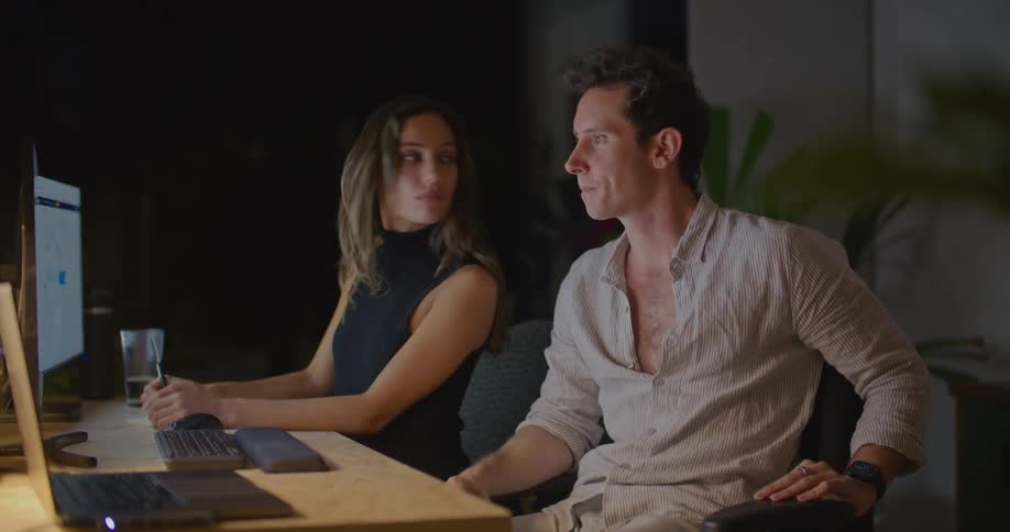 Man points to a monitor as he and a woman sit at a desk and talk