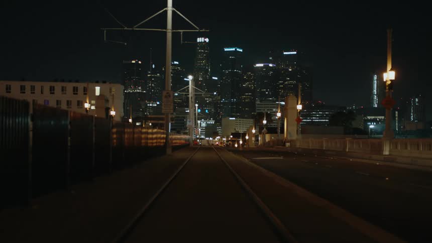 Train tracks next to a street with a city skyline in the distance