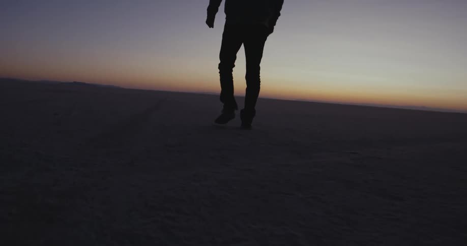 A man walks across soil in a desert area
